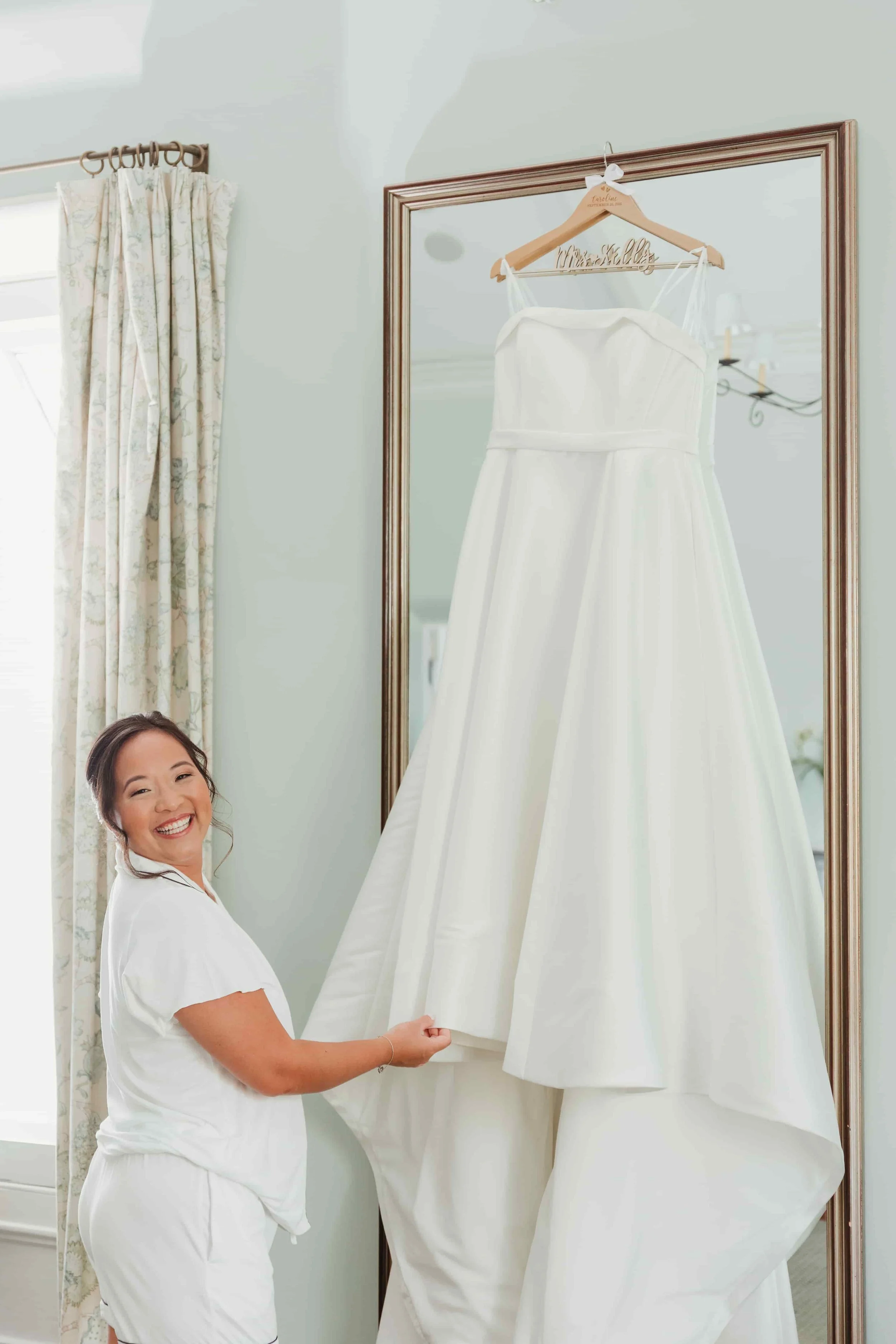 A smiling bride prepares to put on her wedding dress, which is hanging on a mirror in connecticut