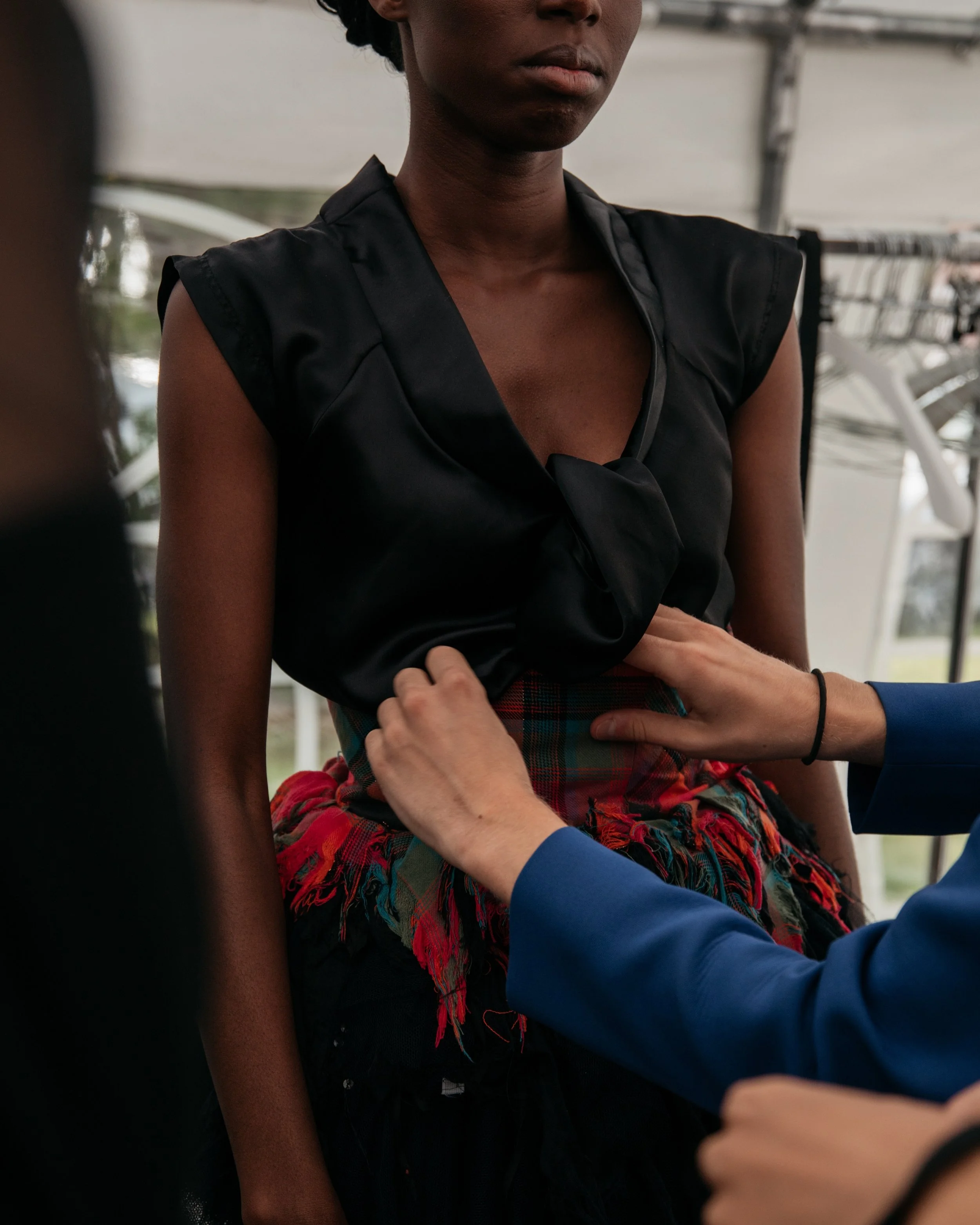 A person wearing a black top is being fitted or adjusted by someone wearing a blue jacket, possibly for a clothing item or uniform.