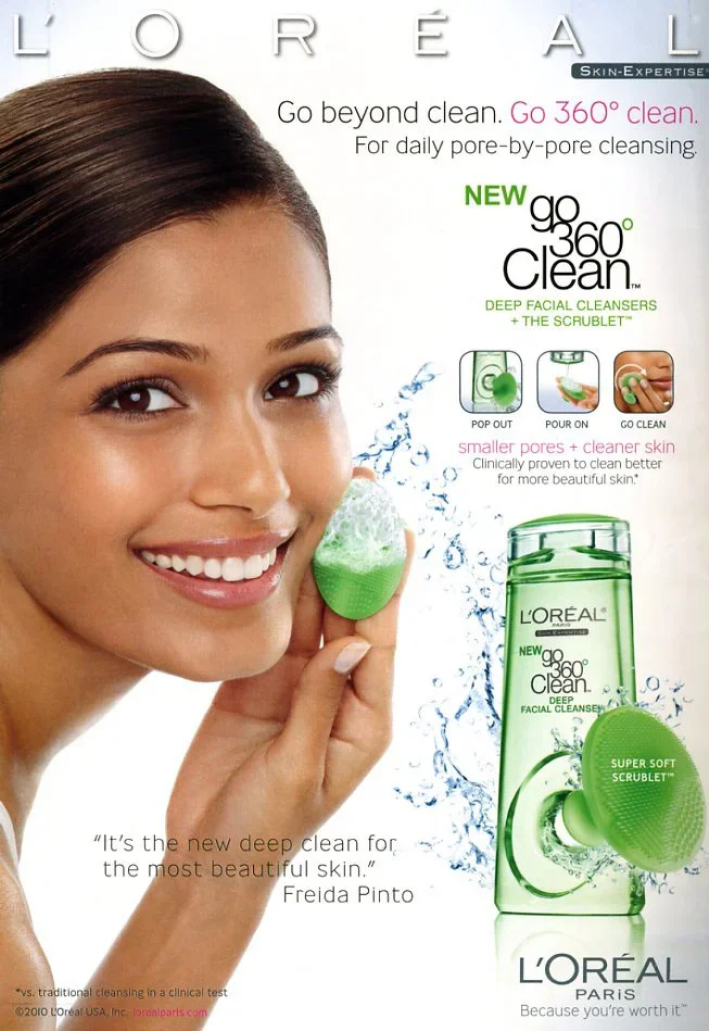A woman holding a green facial cleansing product, smiling, with a box of L'Oreal Go 360 Clean Deep Facial Cleanser and Scrubber beside her, advertisement for a skincare product.