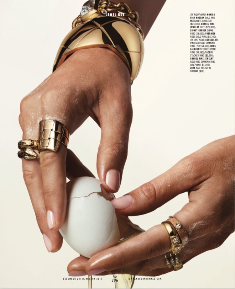 Close-up of hands with jewelry cracking a white egg for decoration, featuring rings and bracelets, against a plain background.