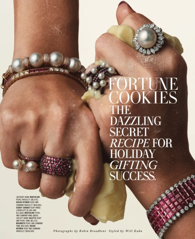 Close-up of two hands wearing jewelry, including pearl bracelets, diamond rings, and ruby rings, holding a cookie with white chocolate chips. The image appears to be a jewelry advertisement with a text overlay.
