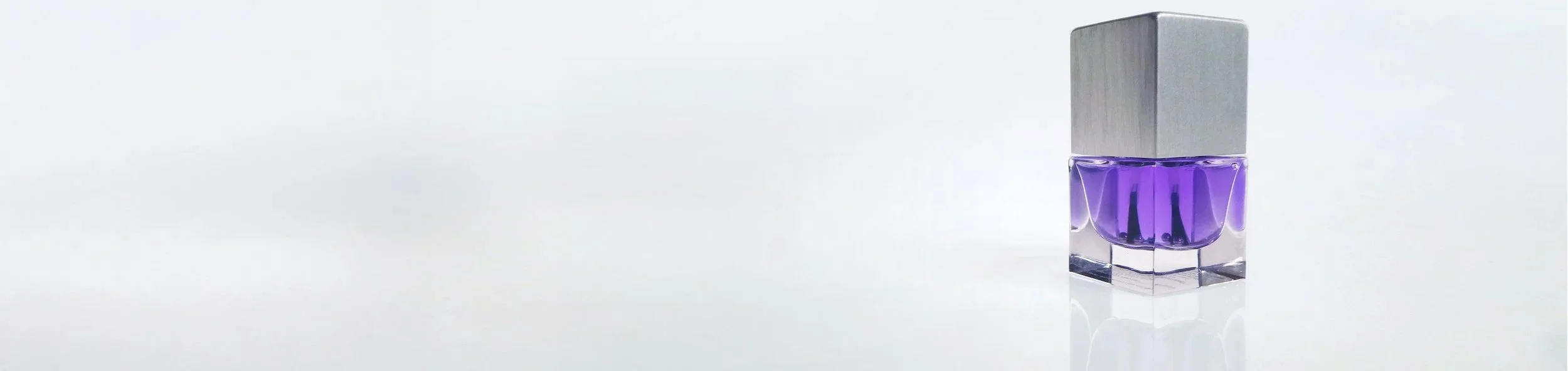 A bottle of purple nail polish with a silver cap, placed on a white surface against a plain white background.