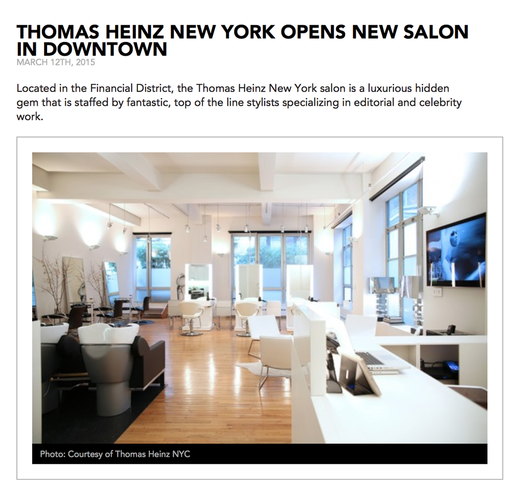 Interior view of a modern, bright, and spacious hair salon with white walls and furniture, wooden flooring, large windows, and wall-mounted television.
