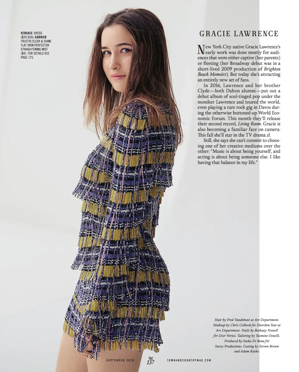 A young woman in a colorful, patterned dress with fringes, standing sideways and looking at the camera in a magazine article layout.