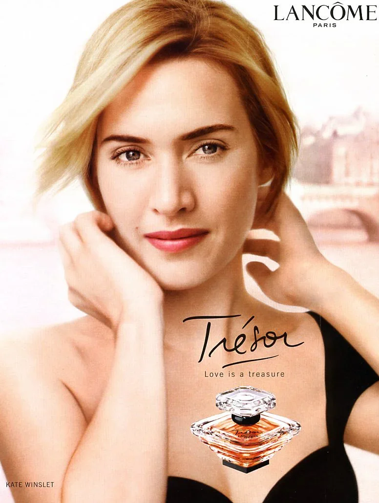 A woman with short blonde hair looking at the camera, with hands near her face. The image features a perfume bottle and the logos of Lancôme and Trezor.