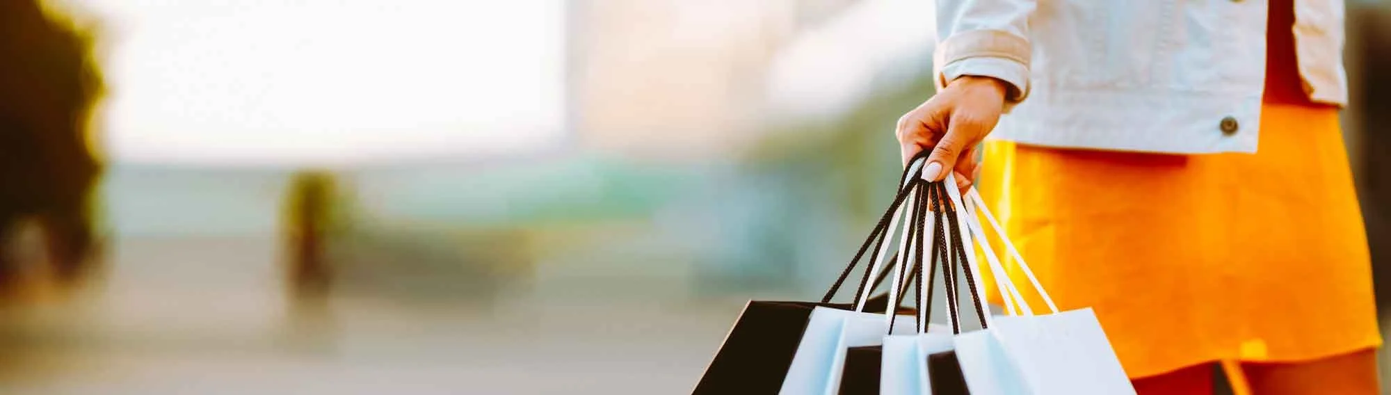 Person holding shopping bags outdoors, with a blurred background.