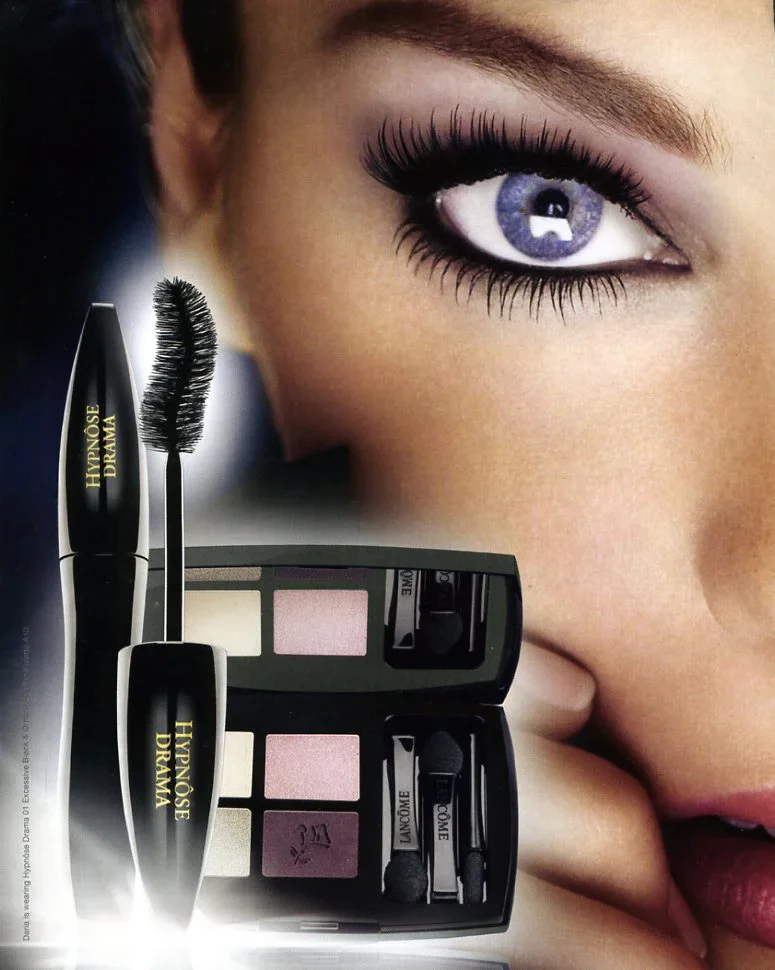 Close-up of a woman's face with makeup, nail polish, and eye contact visible, alongside eye makeup products including mascara, eyeshadow palette, and eyeliner.
