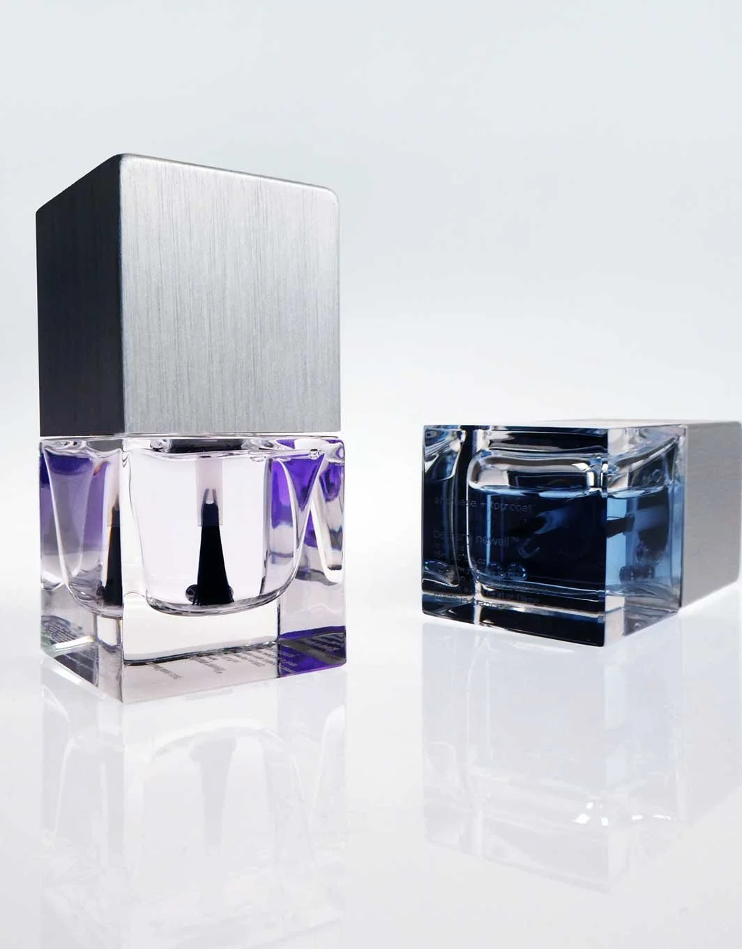 Two luxurious perfume bottles with metallic caps, one with a purple liquid and the other with a blue liquid, placed on a white surface with reflections.