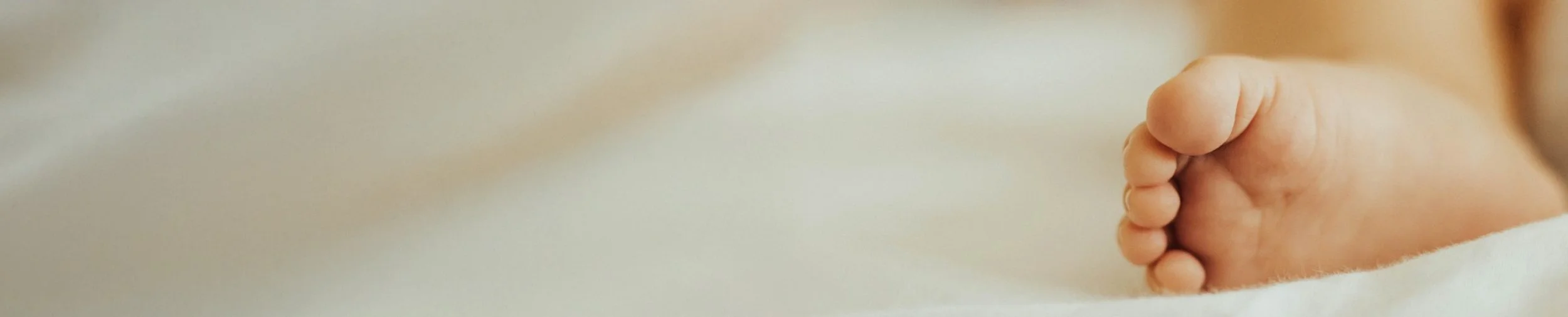 Close-up of a baby's foot resting on a soft, light-colored surface.