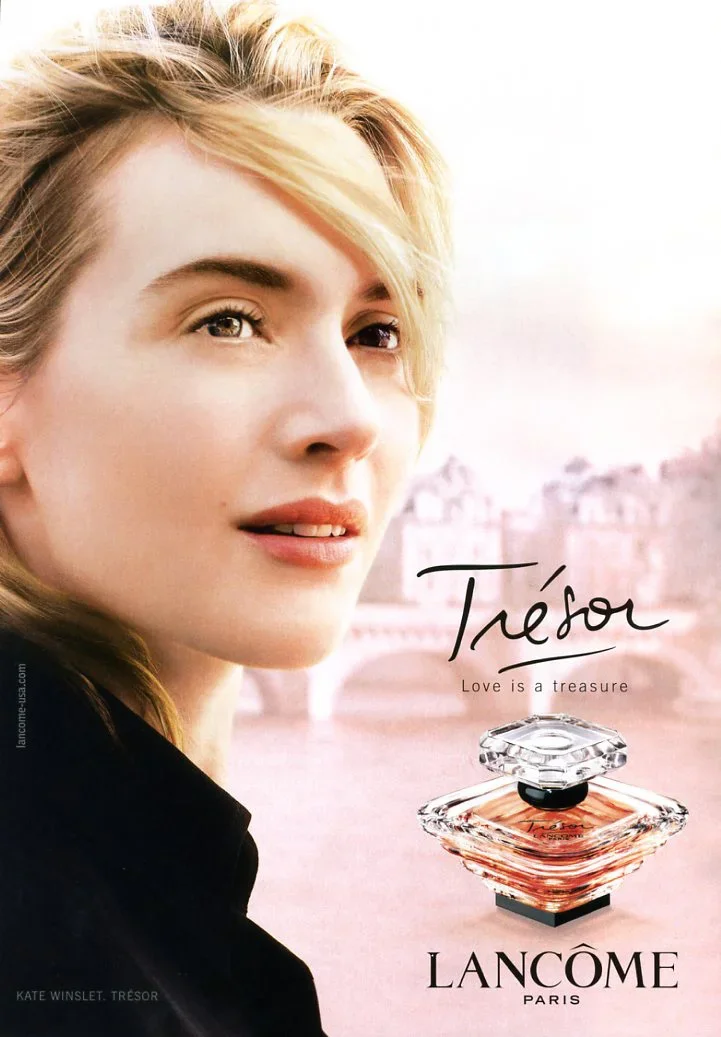 Close-up of a woman with blonde hair, with a blurred cityscape background and a perfume bottle in the foreground. The text reads 'Trésor, Love is a treasure,' and the brand is Lancôme Paris.