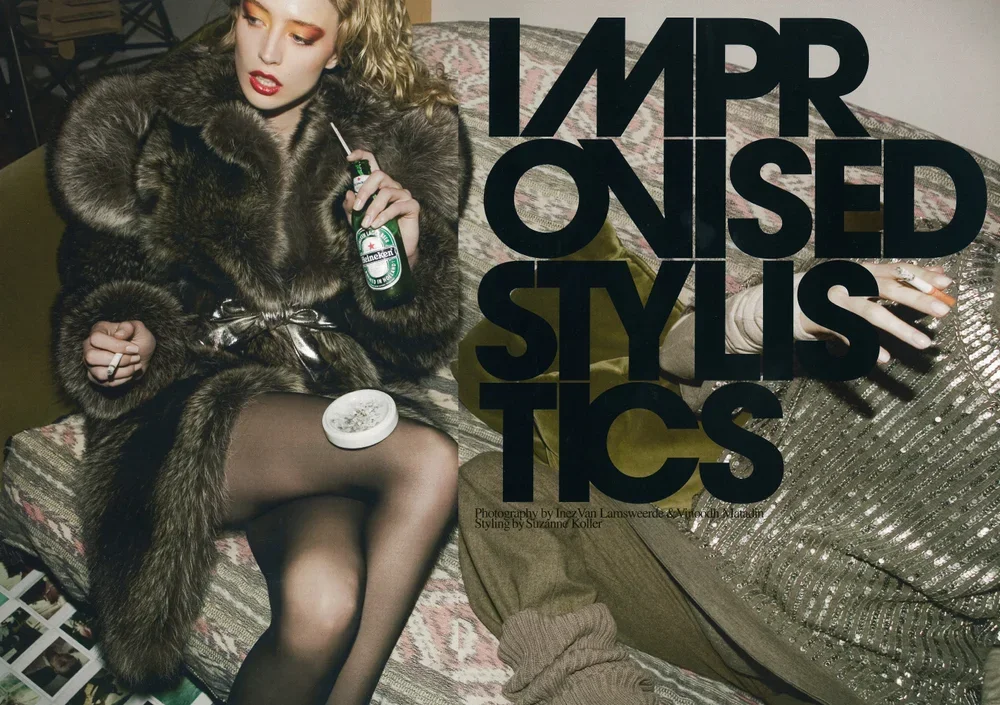 A woman with curly blond hair, wearing a fur coat, black stockings, and dark makeup, sits on a vintage sofa with a drink and an ashtray. Large text reads 'IMPROVISED STYLISTICS' over the image.
