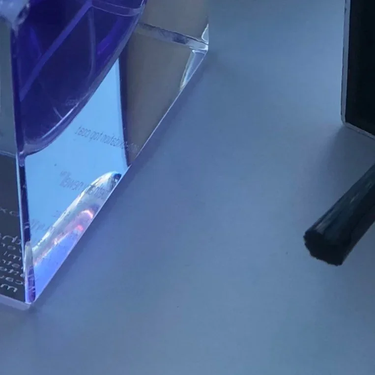 Close-up of a desk with a purple and clear acrylic organizer, a black object, and a surface with a faint reflection.