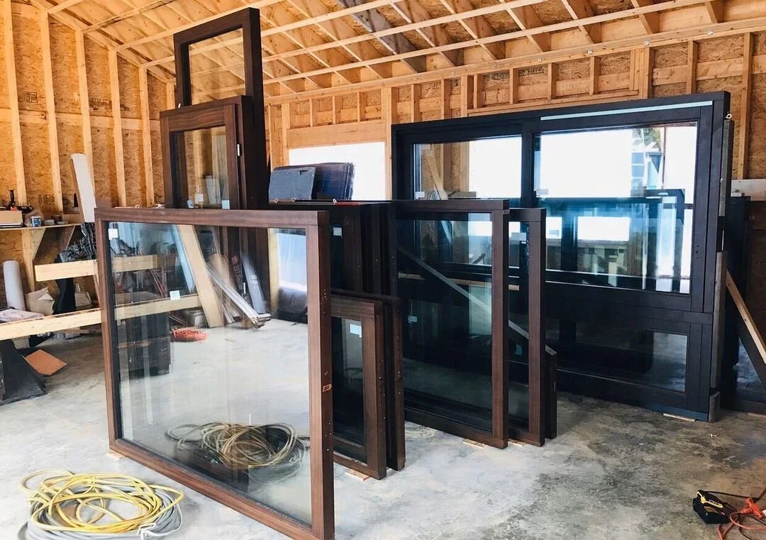 A workshop with various windows and glass panels leaning against a wall in a partially constructed wooden building.