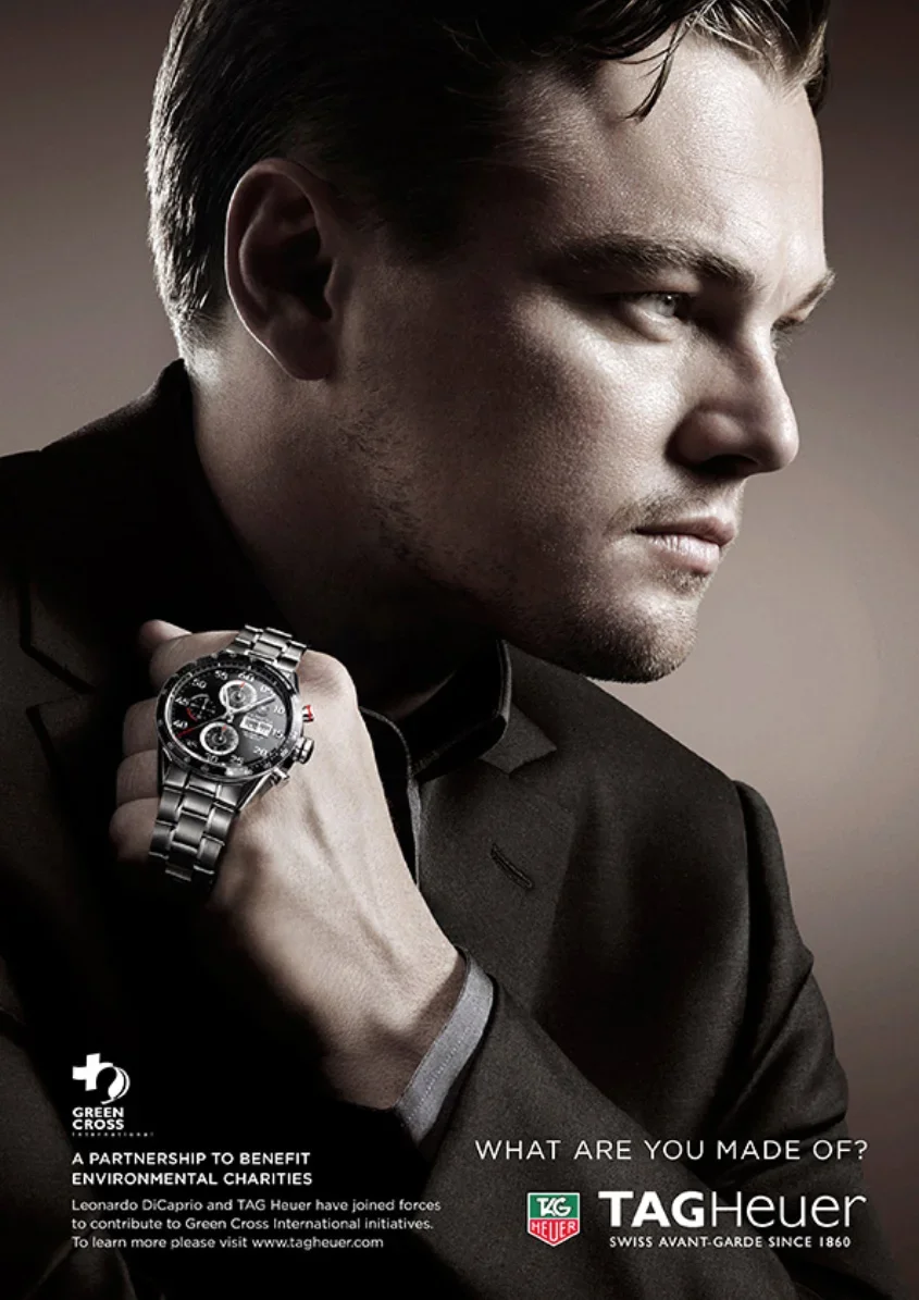 A man wearing a black suit and a TAG Heuer watch on his wrist, with a serious expression, looking to the side.