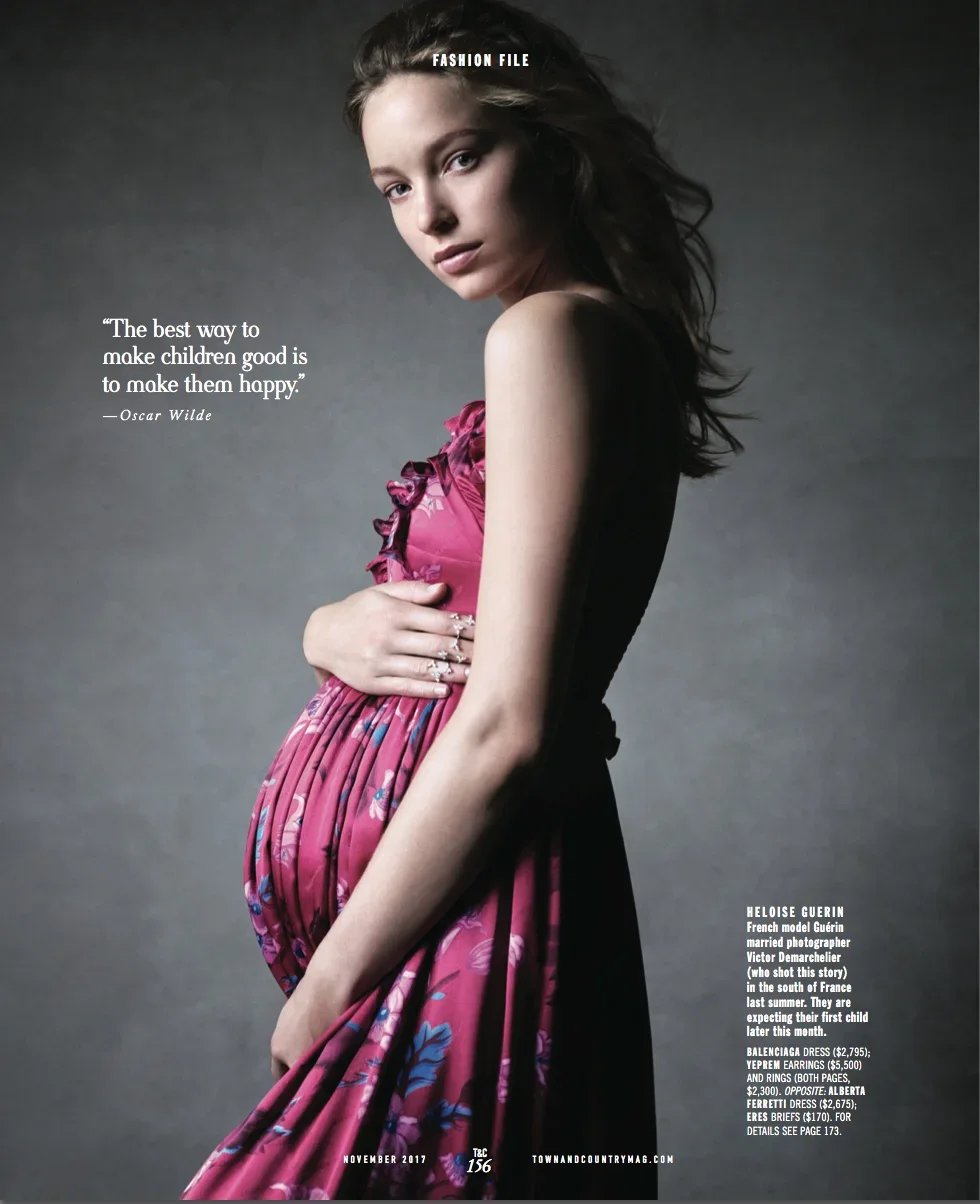 Young woman with long hair looking at the camera, wearing a pink floral dress, standing against a gray background.