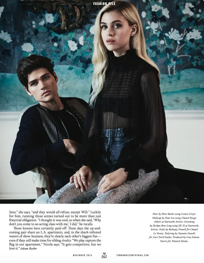 A young man and woman in fashionable clothing posing indoors with a painted floral backdrop.