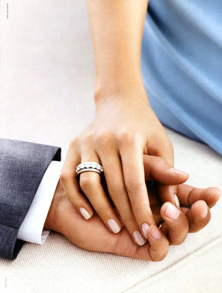 Close-up of a woman's hand with a wedding ring, holding a man's hand, during a wedding or engagement ceremony.