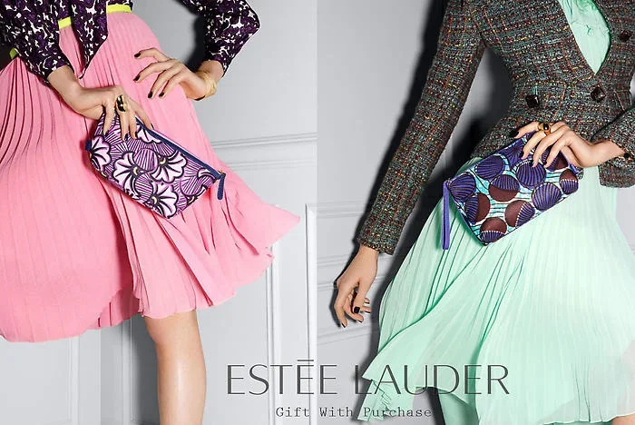 Two women dressed in retro-style dresses holding colorful clutch purses, with the Estée Lauder logo and text 'Gift With Purchase' visible.