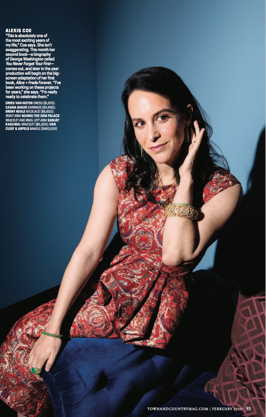 A woman with dark hair, wearing a red patterned dress, sitting on a dark blue chair with a purple pillow, touching her face, against a blue background.