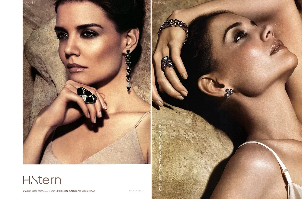 Two women with dark hair and jewelry, one with a long earring and ring, the other with earrings, a bracelet, and rings, posing against a rocky background.