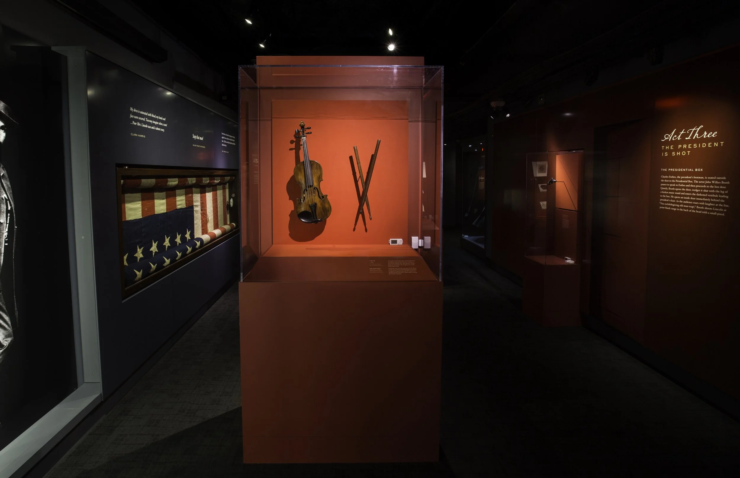A display case with a violin and two crossed batons inside, part of a museum exhibit about American history.