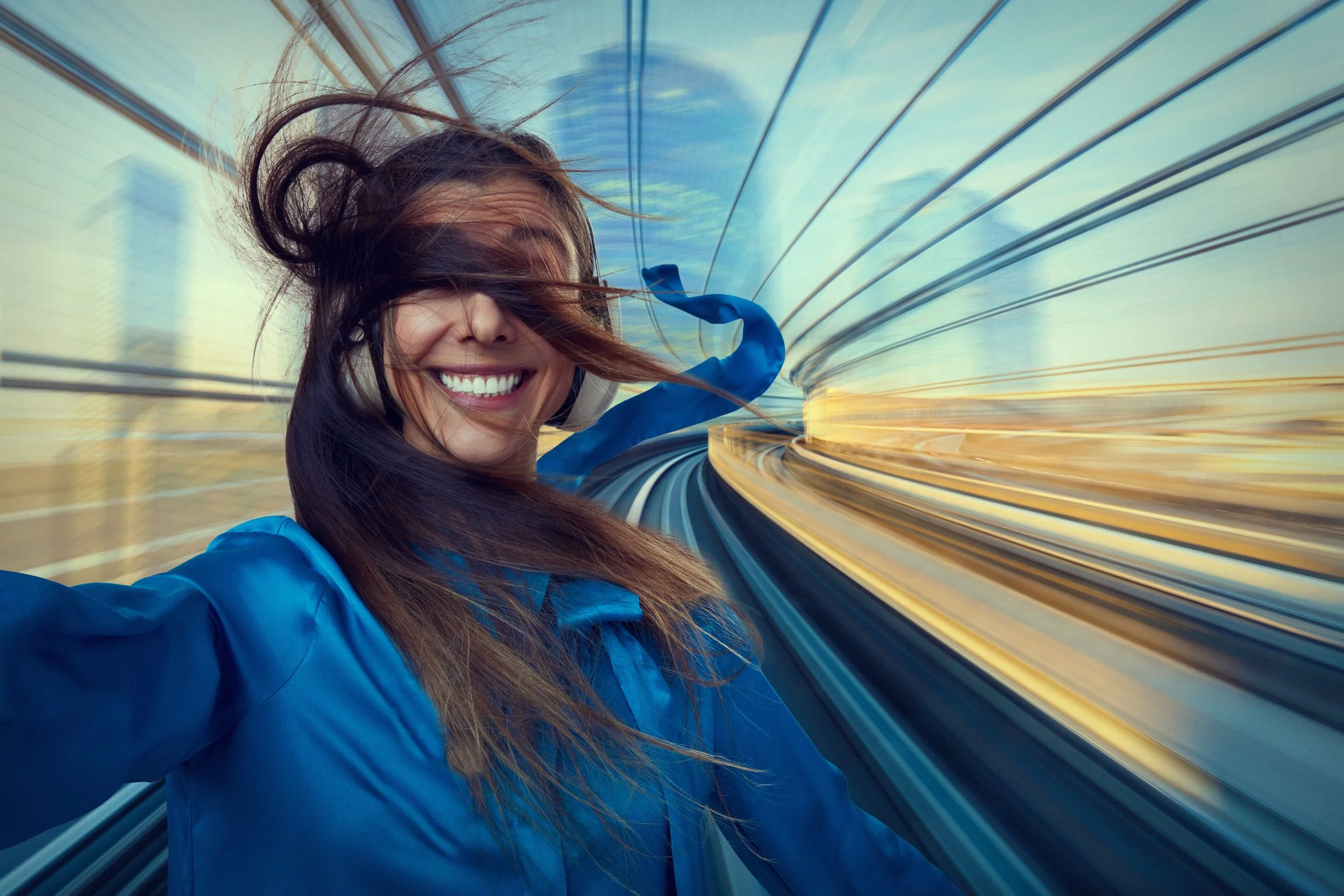A woman smiling with windblown hair on a high-speed train with blurred landscape in the background.