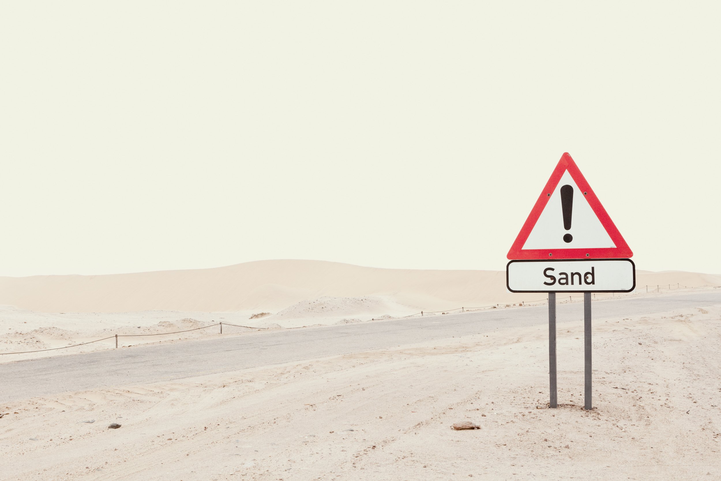 A warning sign in a desert landscape indicating the presence of sand.