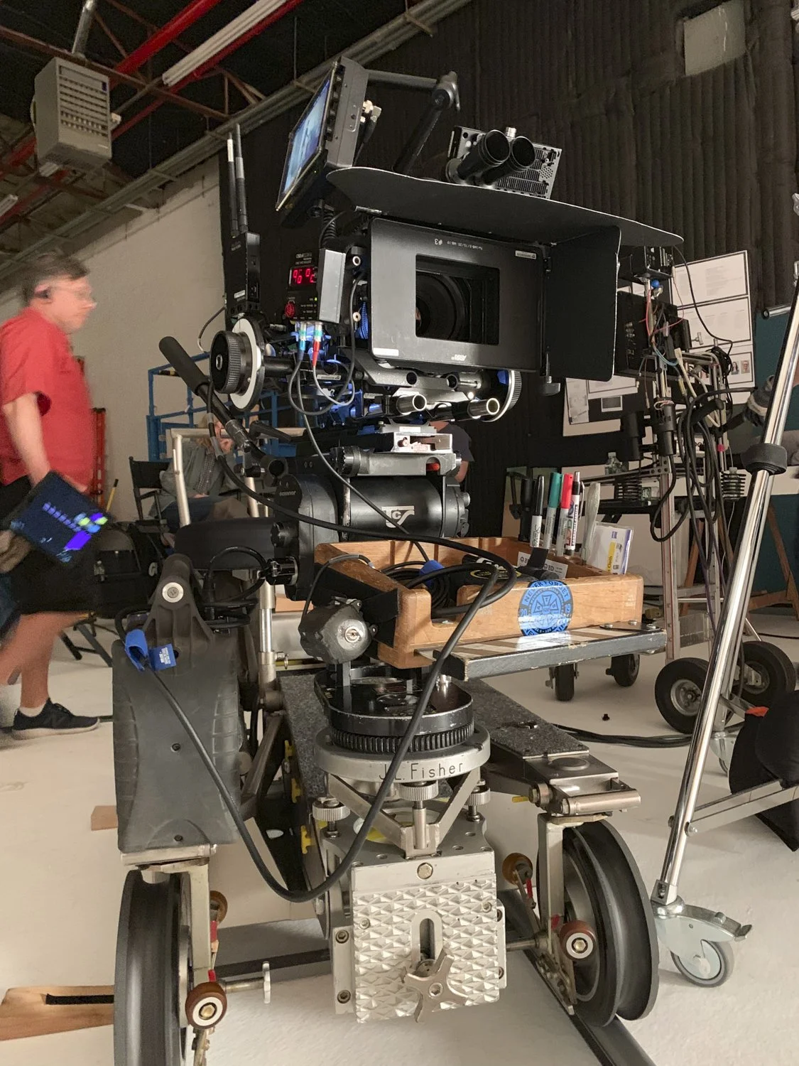 A professional film camera mounted on a dolly in a film studio, with a person holding a clapperboard blurred in the background.