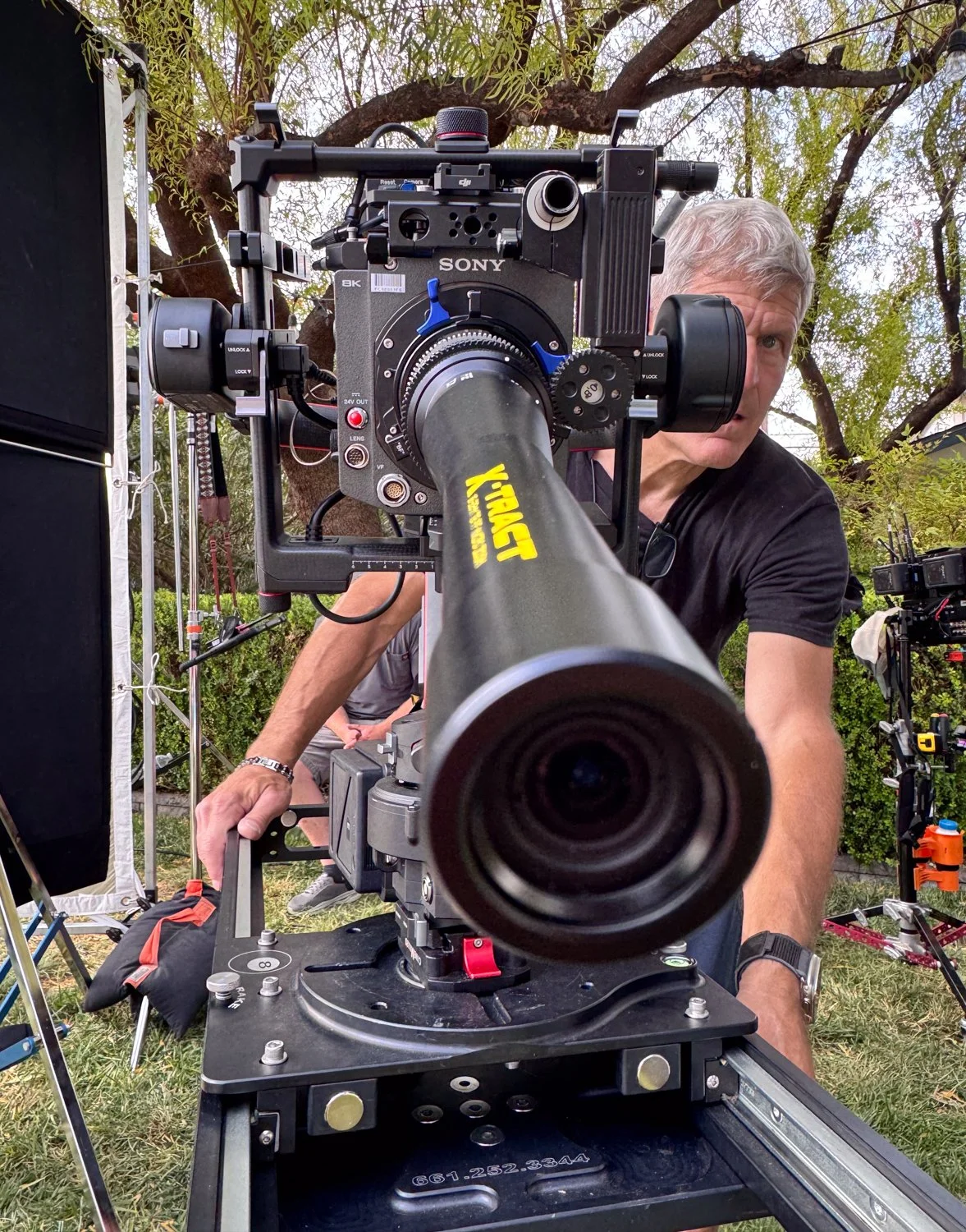 Close-up view of a professional cinema camera mounted on a tripod, with a man adjusting it outdoors.