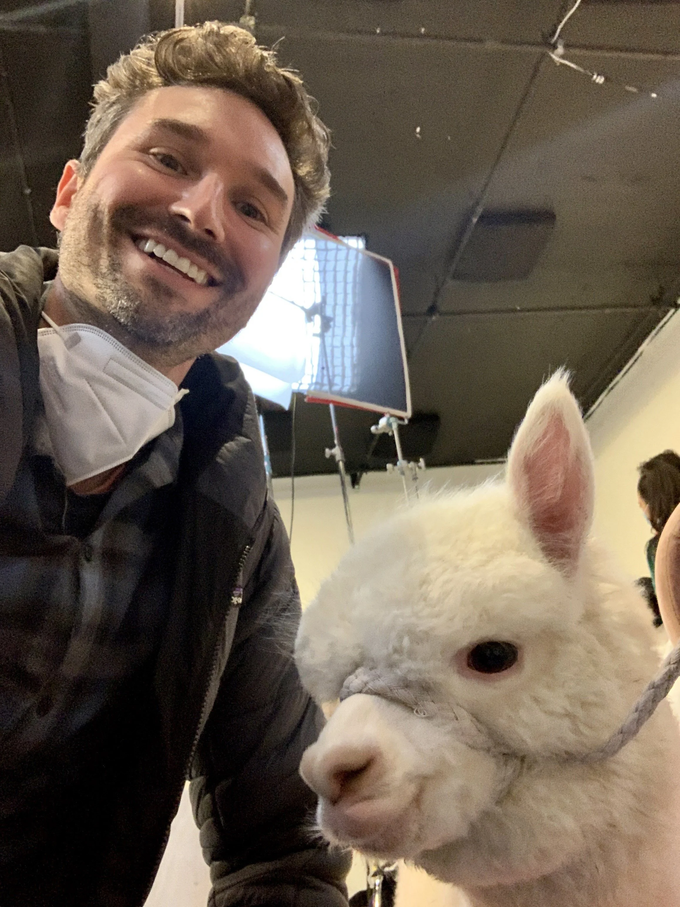A man taking a selfie with a white alpaca.