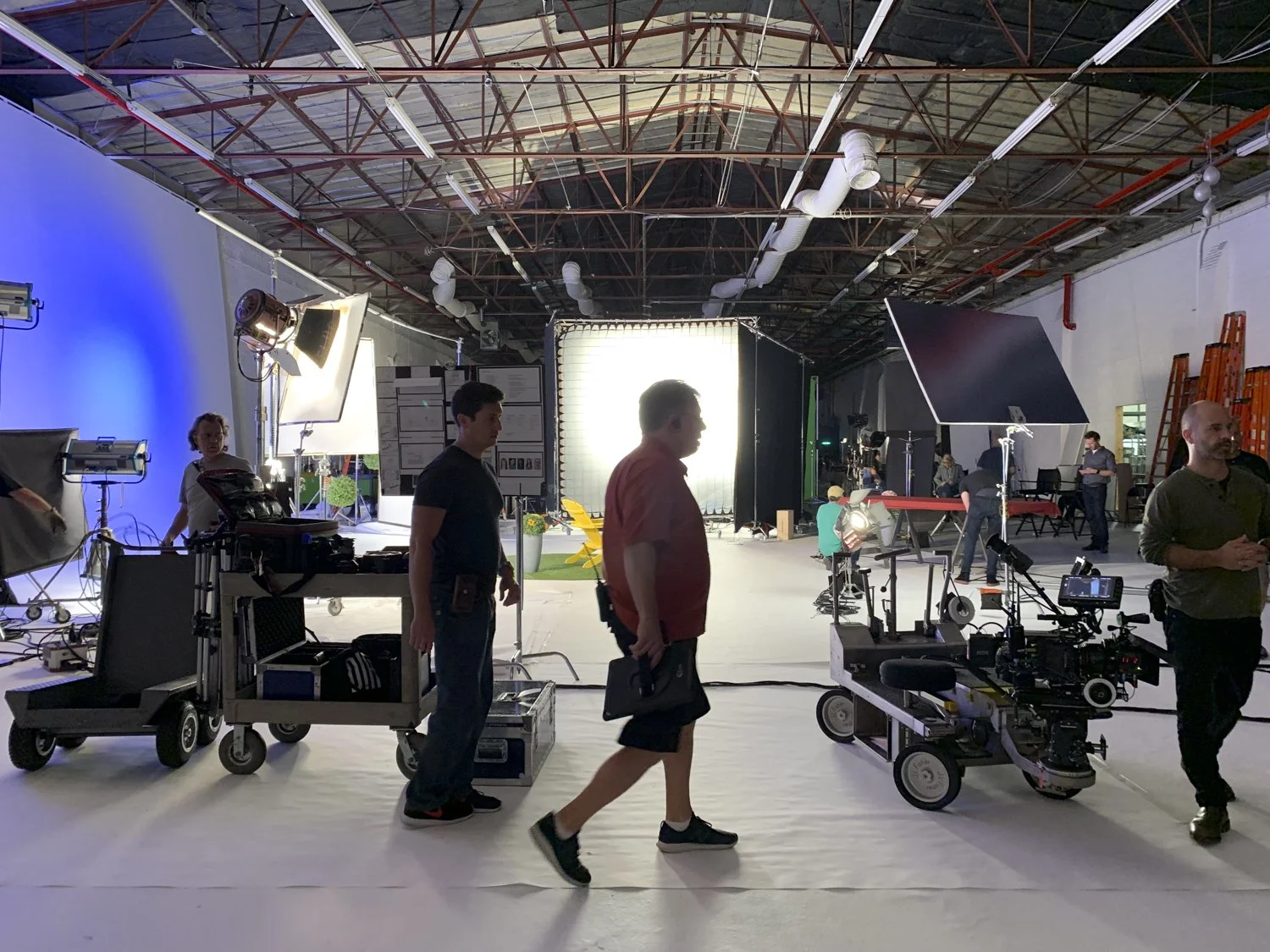 Film or photography studio with lighting equipment, cameras, and crew preparing for a shoot, with a backdrop and various filming gear.