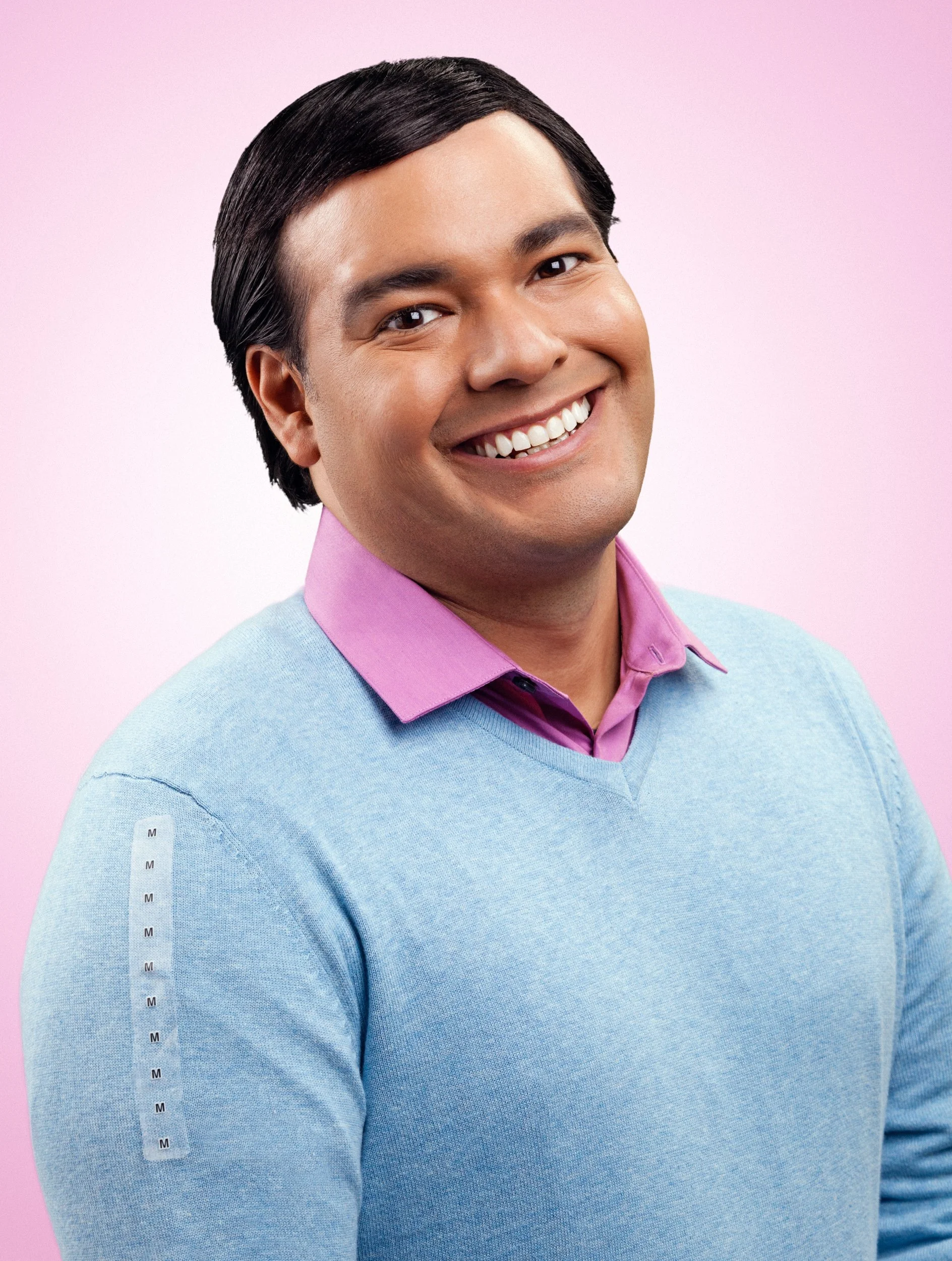 Smiling man with dark hair, wearing a pink collared shirt under a light blue sweater, standing against a pink background.