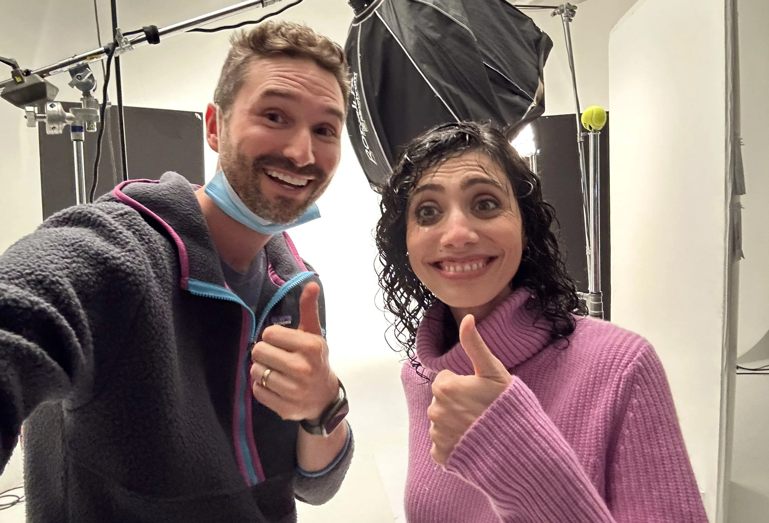 Two people giving thumbs up in a studio setting with professional lighting and equipment.