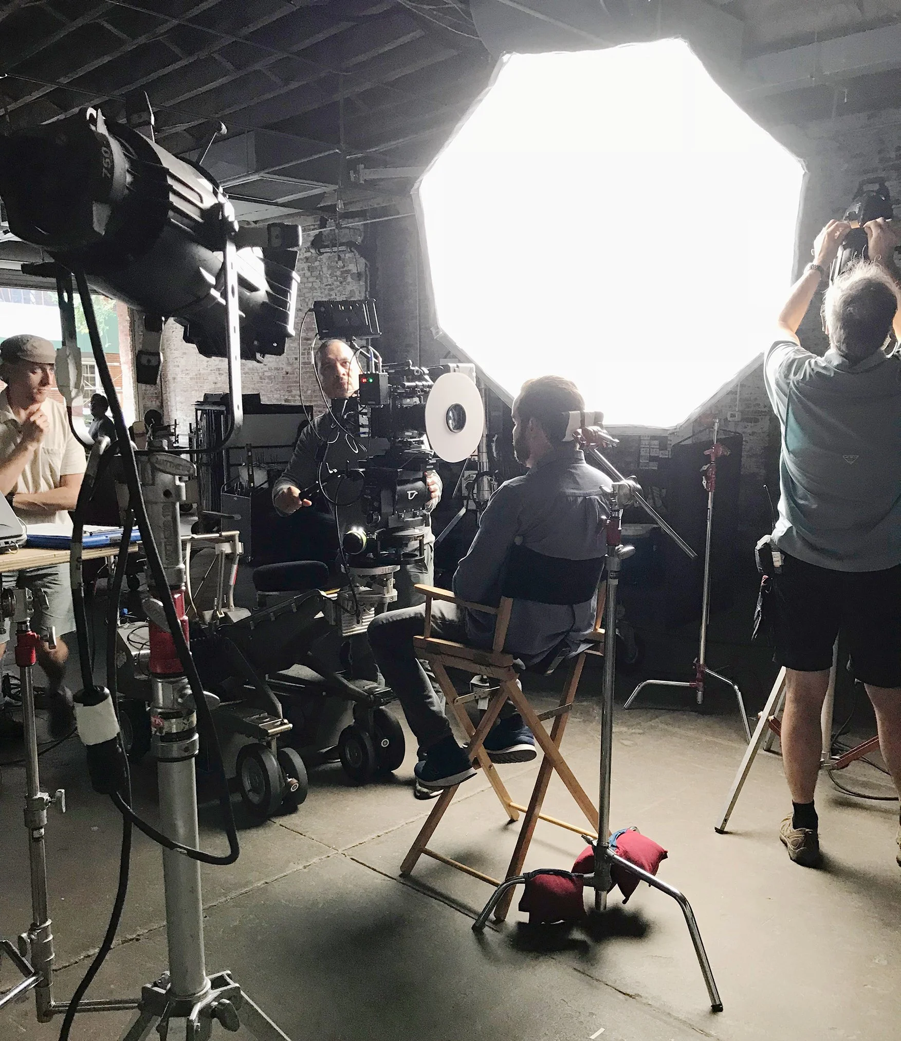 People on a film set with a large lighting setup, camera equipment, and crew members preparing for a shot.