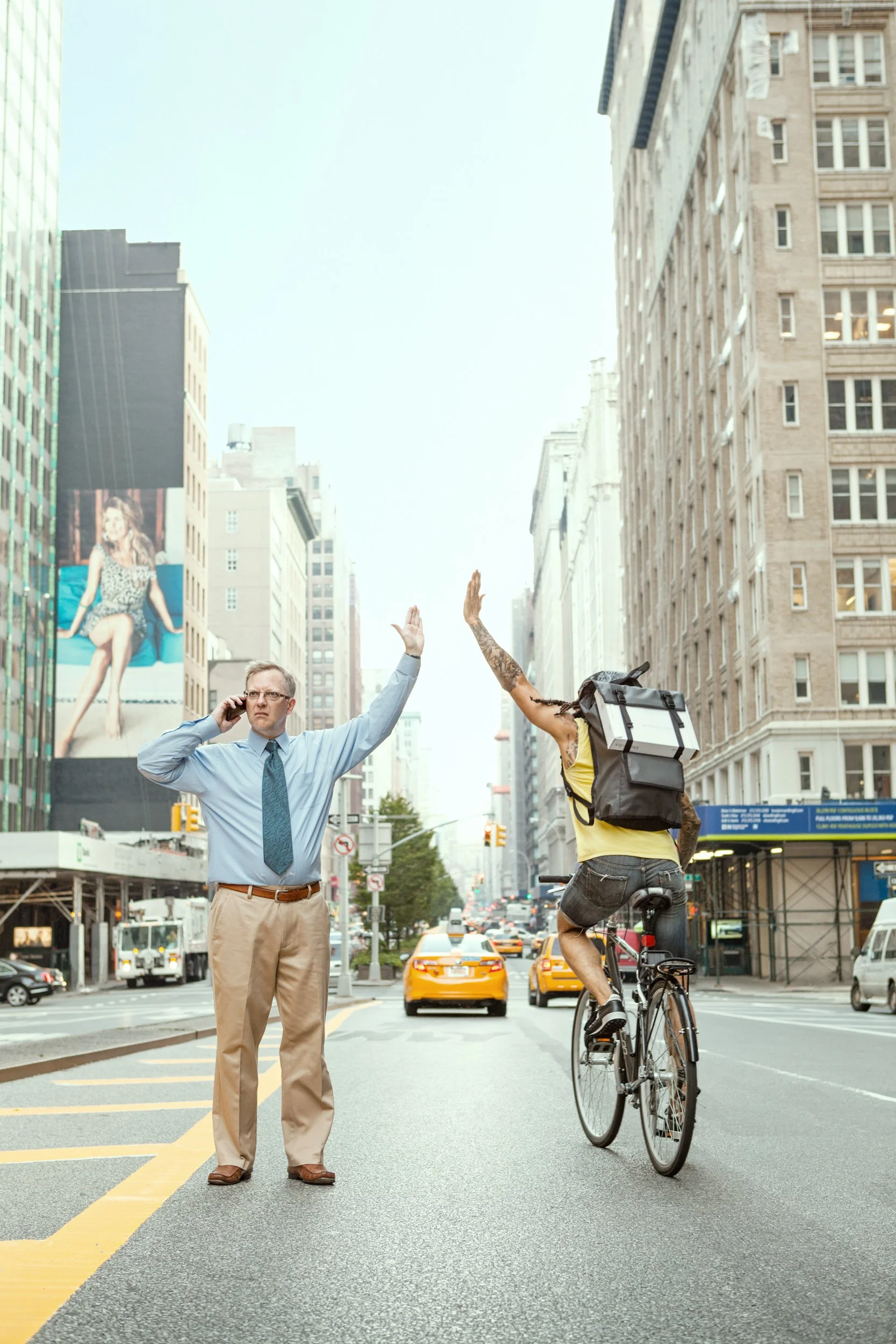 A man in business attire talking on his cellphone while raising his hand, and a woman on a bicycle with a large backpack, high-fiving each other in a city street.
