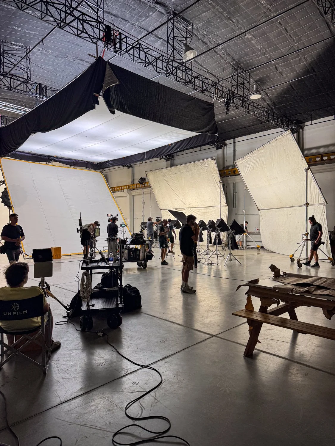 A film studio set with large studio lights and diffusers, multiple crew members working, and equipment on the floor.