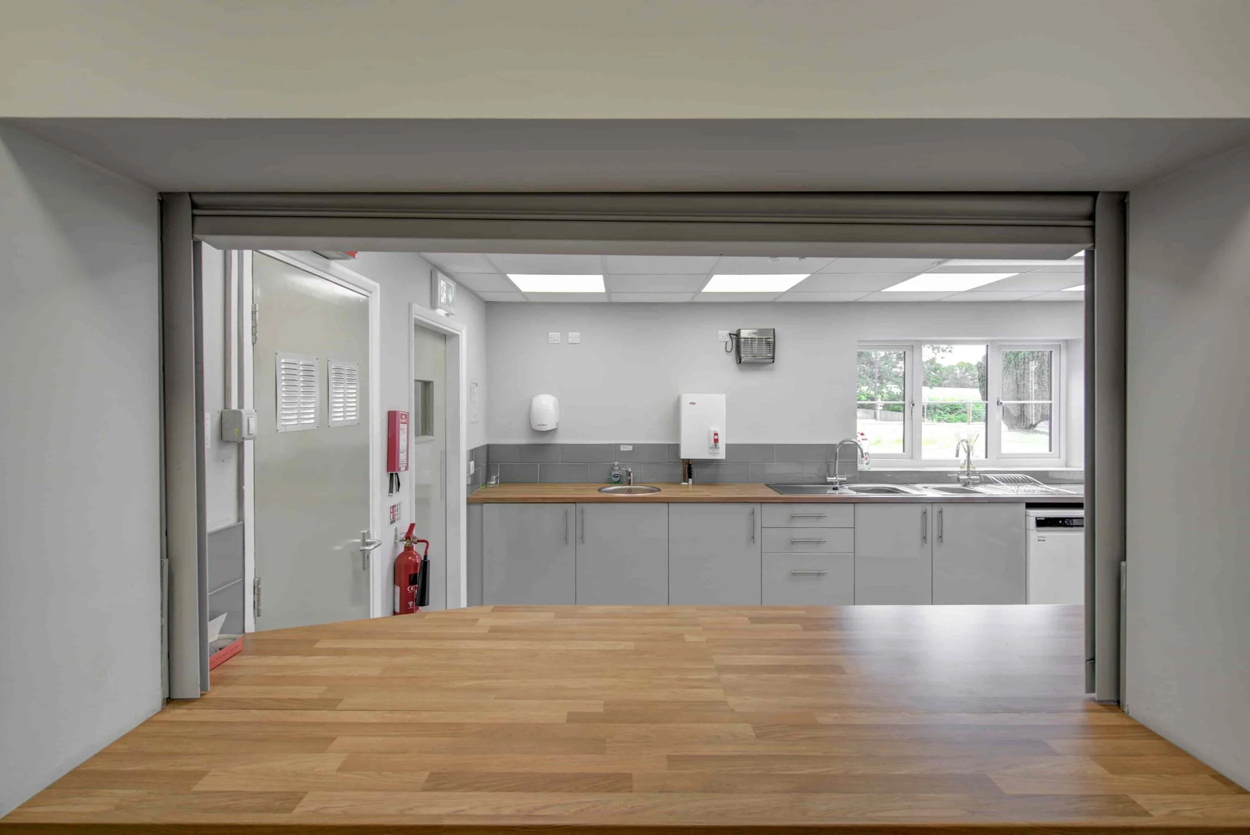 Kitchen with white cabinets and wooden countertop, windows overlooking greenery, tiled backsplash, and various appliances including a sink, dishwasher, and wall-mounted water heater.