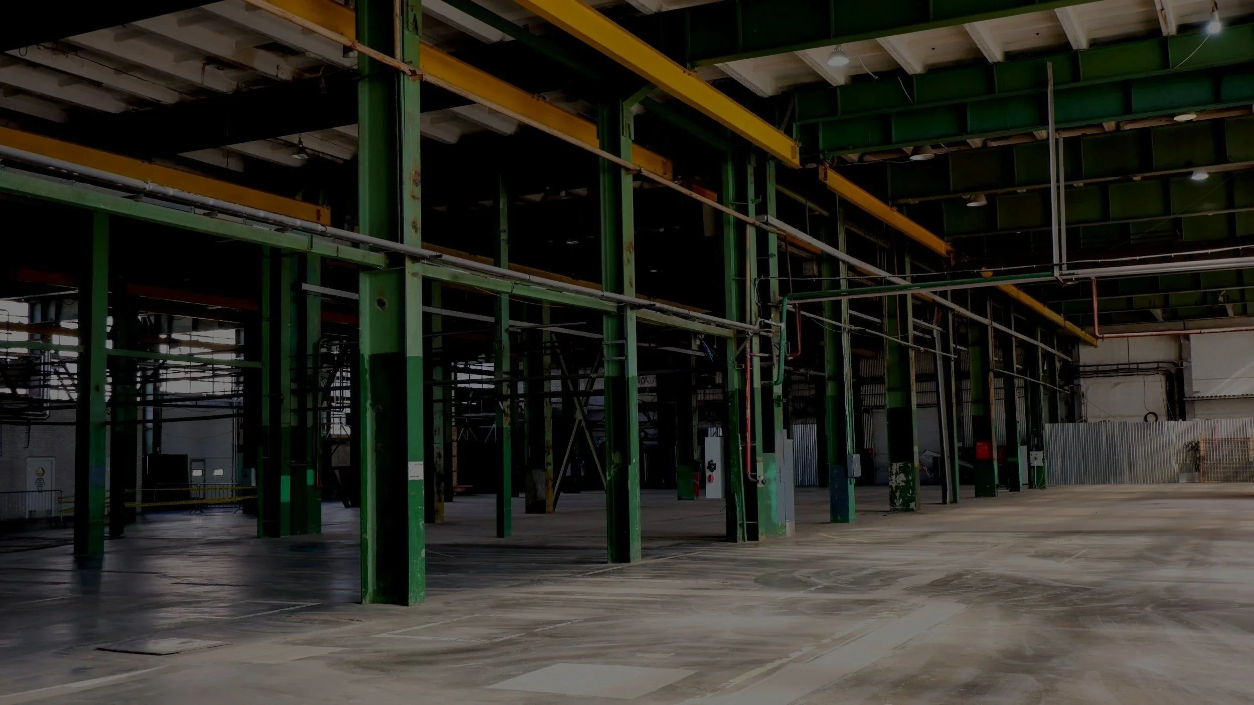 Empty industrial warehouse with green metal support beams and a concrete floor.