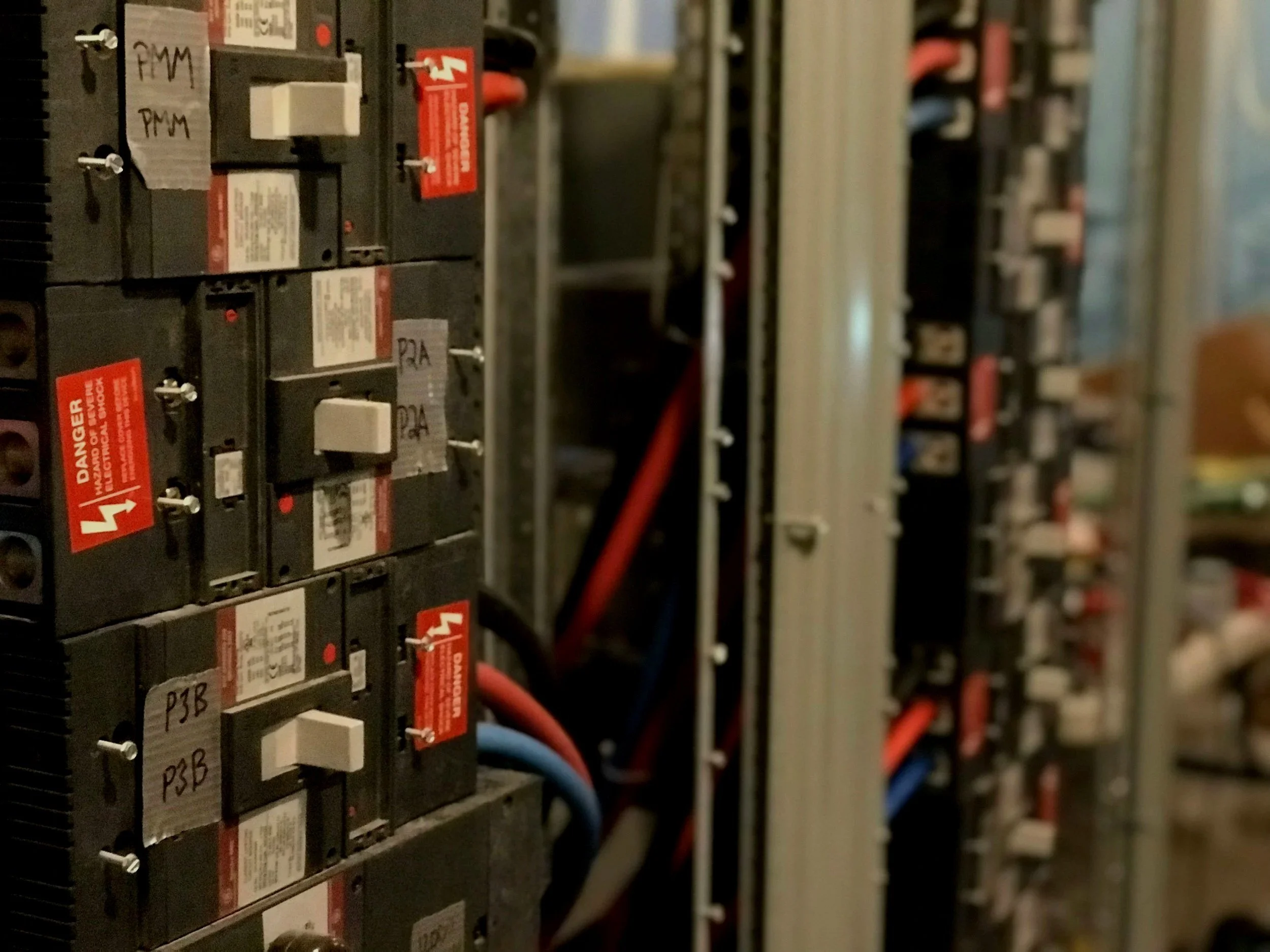 Close-up of electrical circuit breakers with warning labels and wiring in an electrical panel.