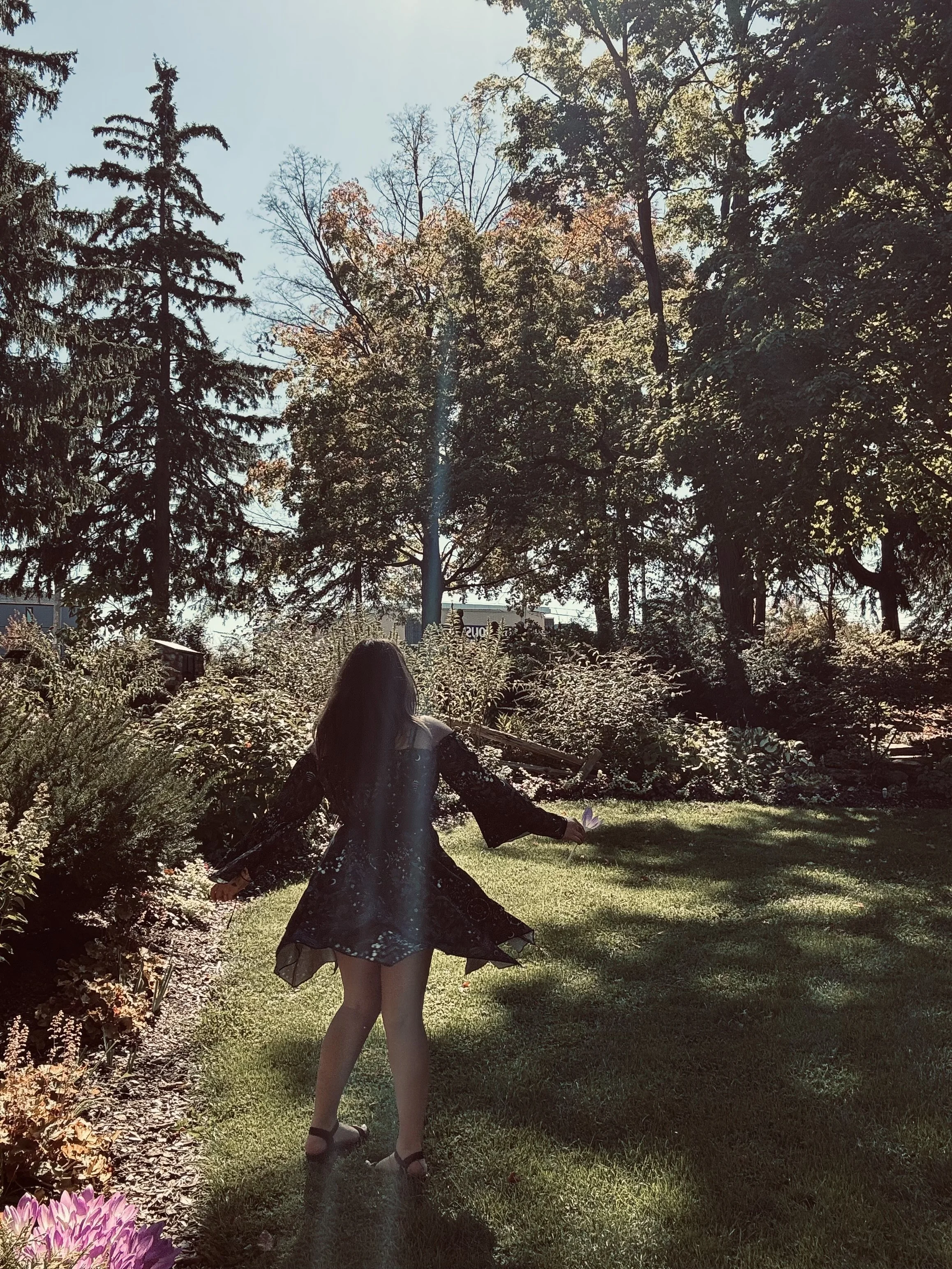 A woman walking through a garden with trees in the background on a sunny day.