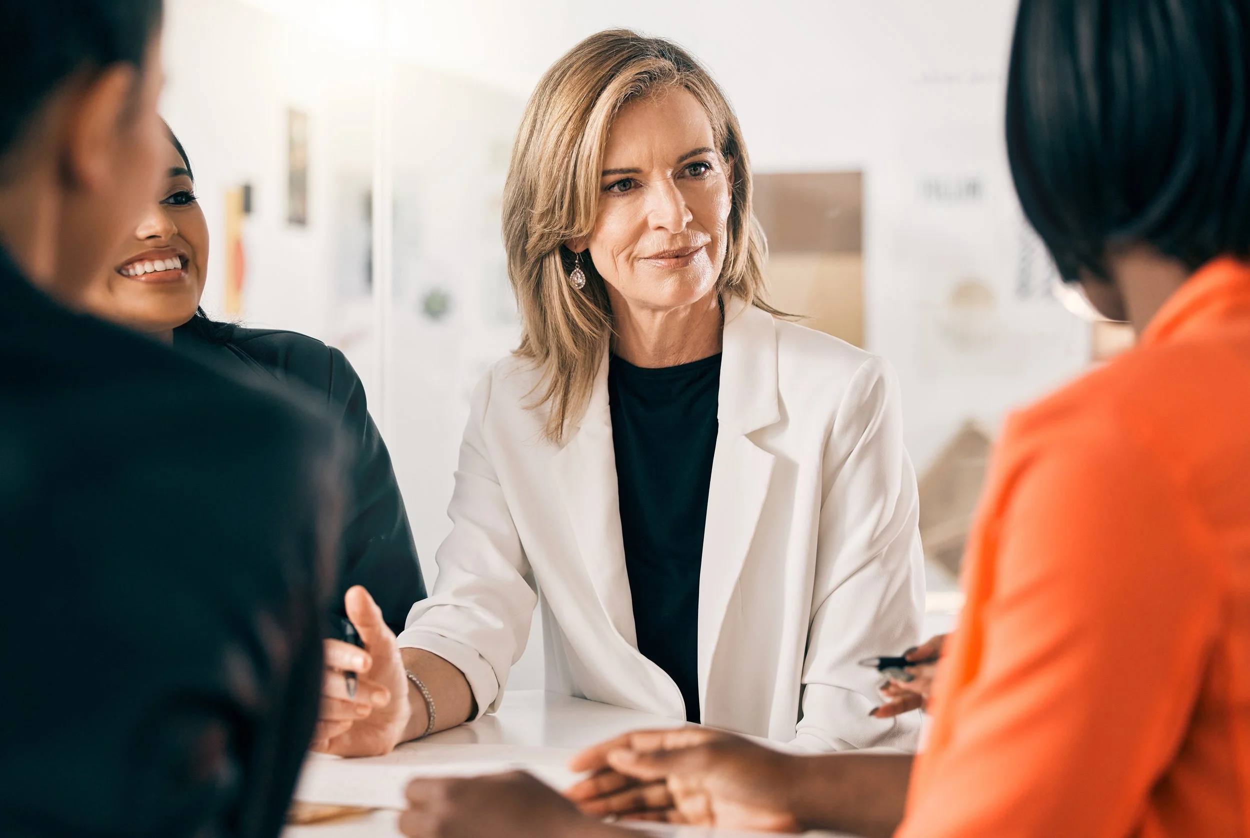 A group of diverse women engaged in a discussion, with one woman in a white blazer listening attentively.