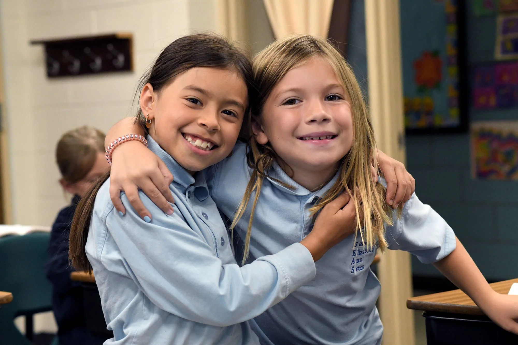 Two girls hugging and smiling in a classroom.