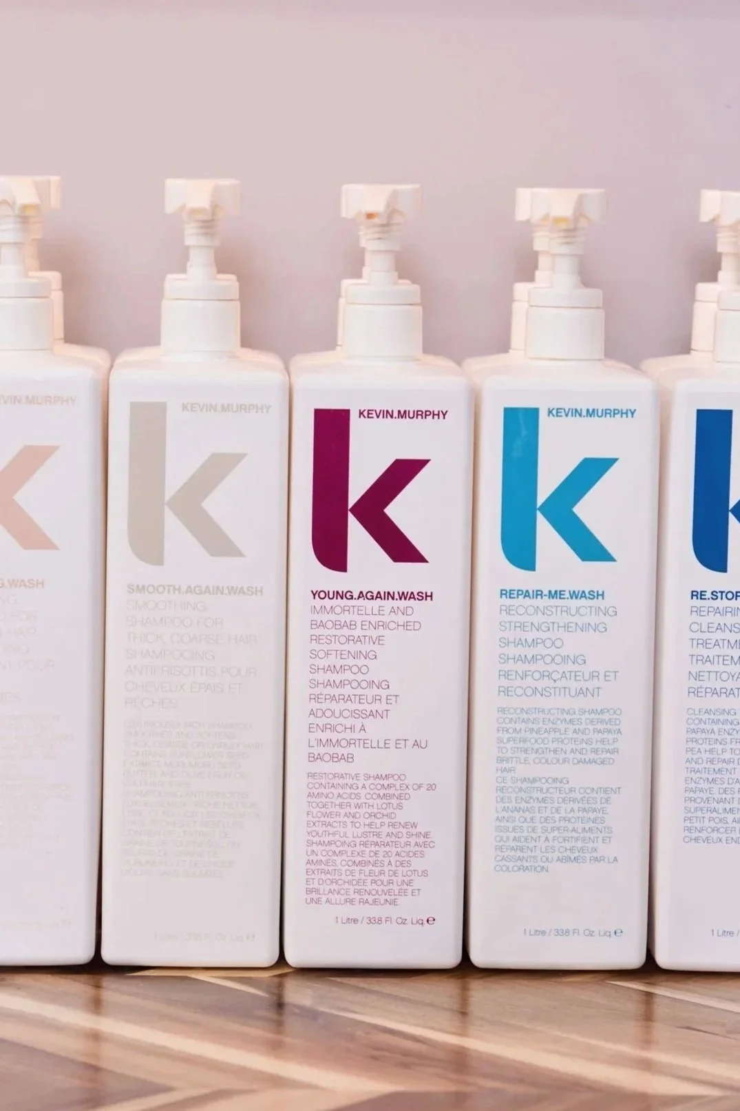 Bottles of Kevin Murphy hair care products arranged on a wooden surface, including shampoos and treatments in various colors and labels.