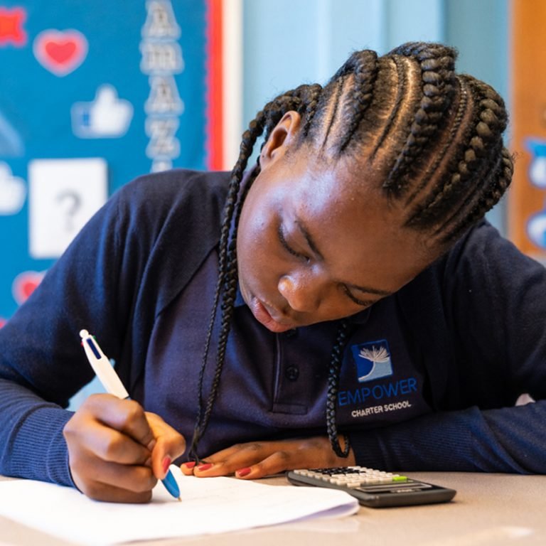 Student working at a desk, writing on paper with a pen, in a classroom setting.