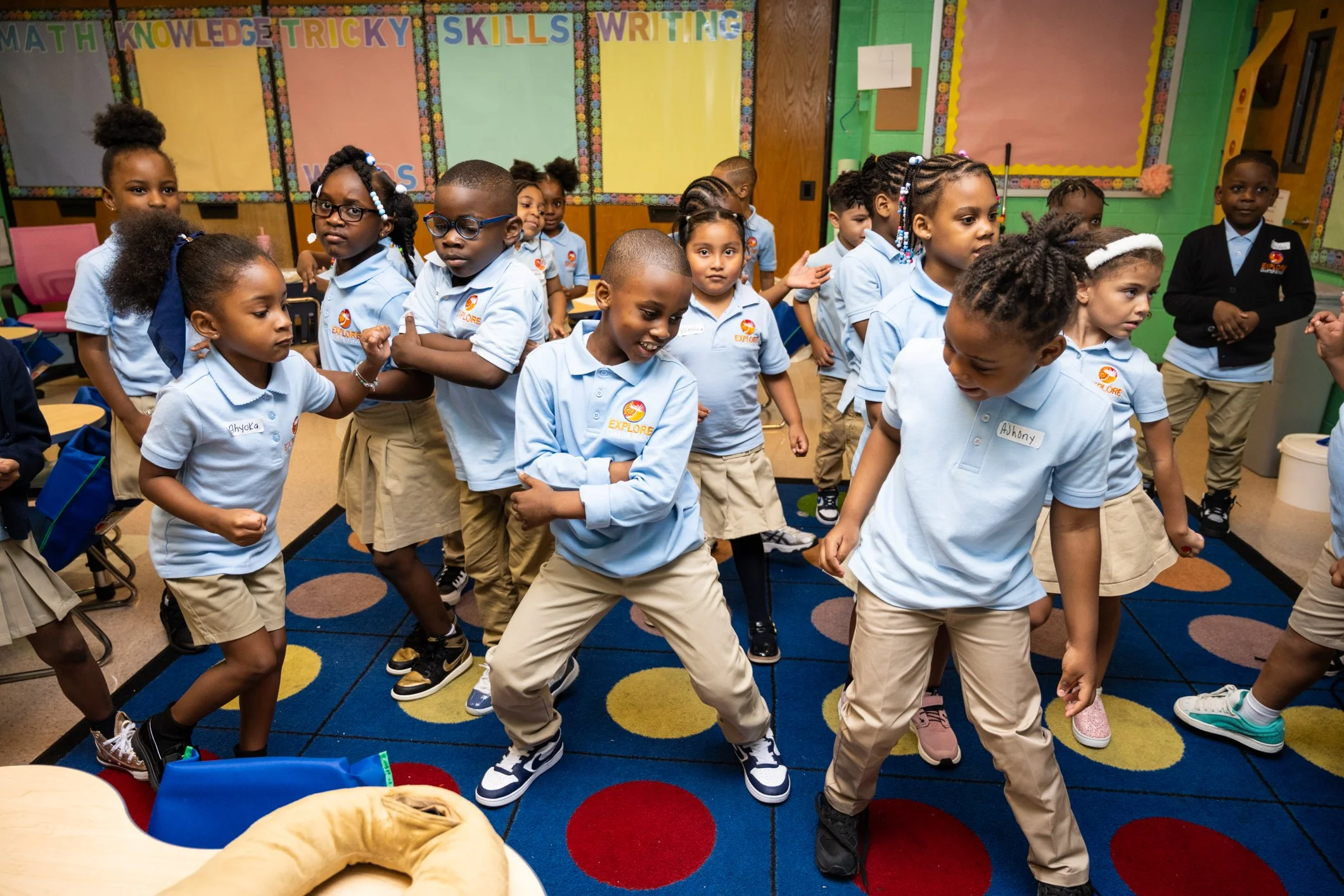 Elementary school children in uniform dancing and having fun in a colorful classroom.