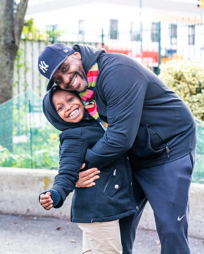 A man and a boy hugging and smiling outdoors.