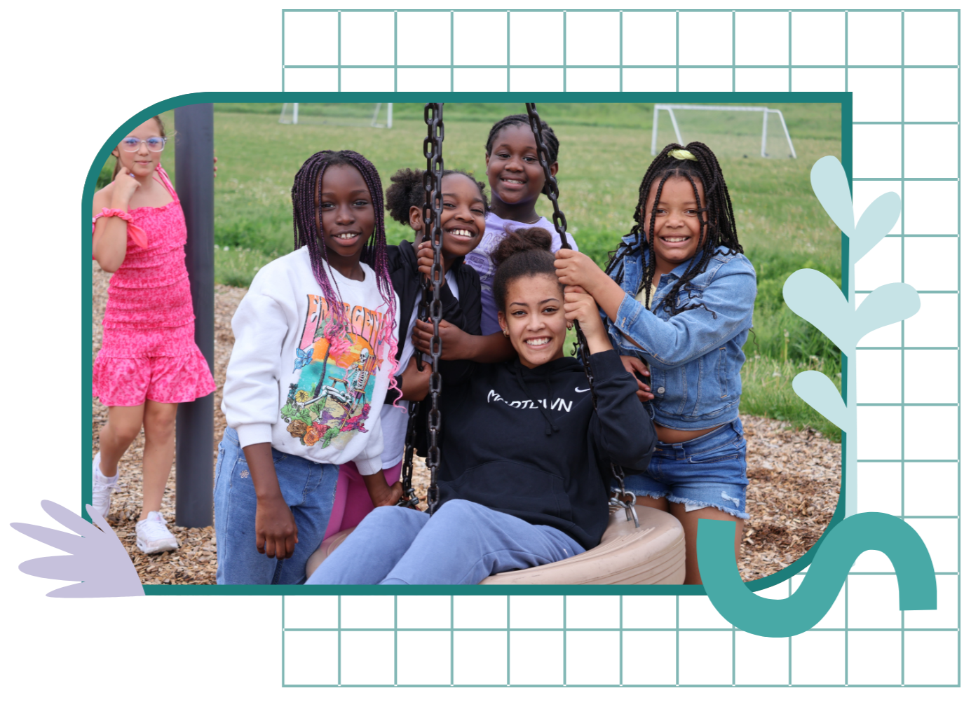 Group of children with a woman on a playground swing, smiling at the camera, outdoors on a grassy field with small goalposts in the background.