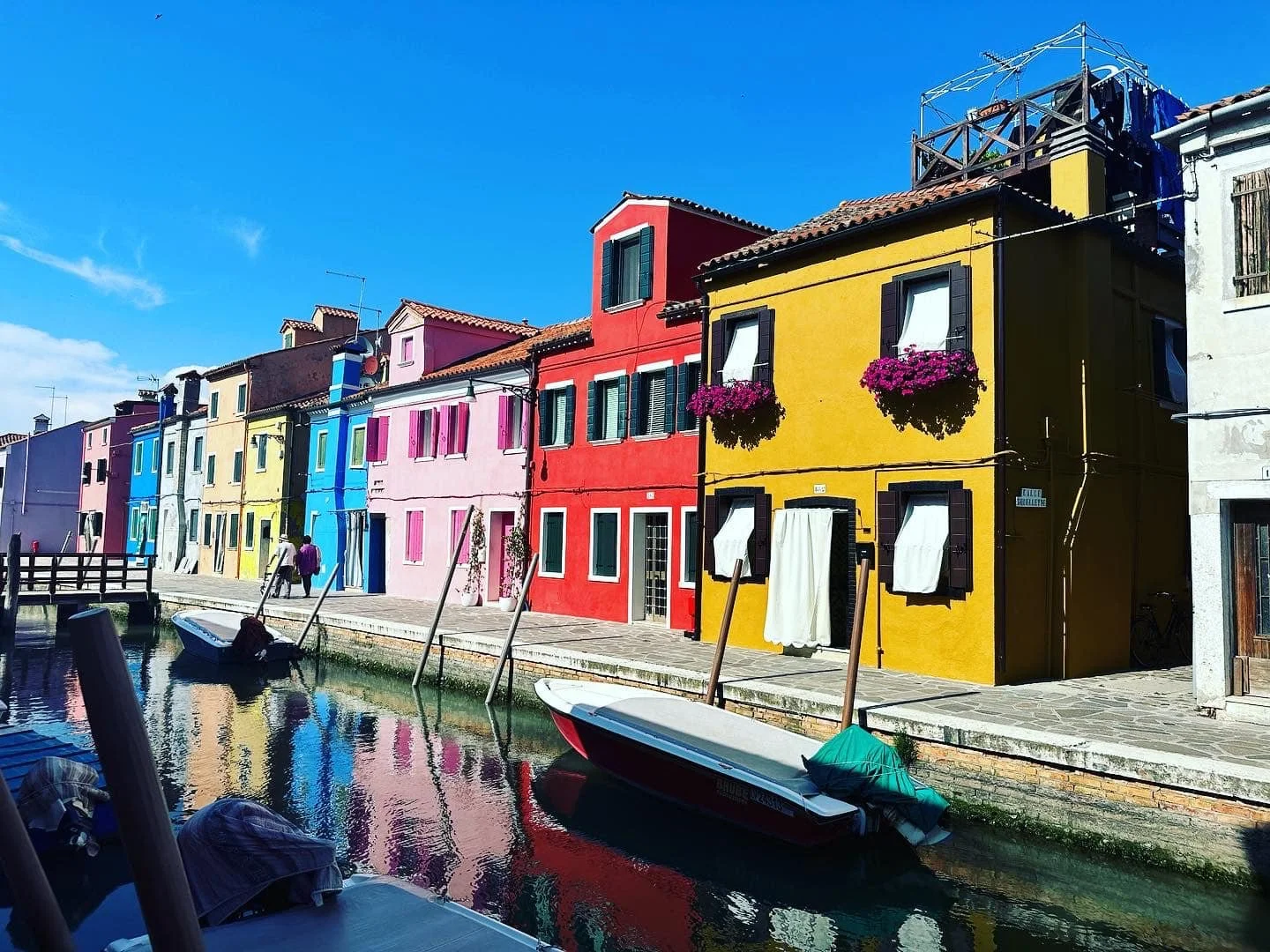 Colorful houses lining a canal with boats afloat and a clear blue sky.