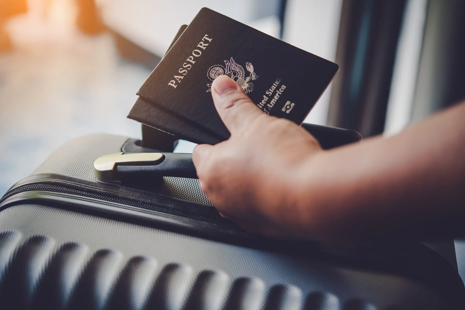 A person holding two United States passports over a checked luggage handle at an airport.