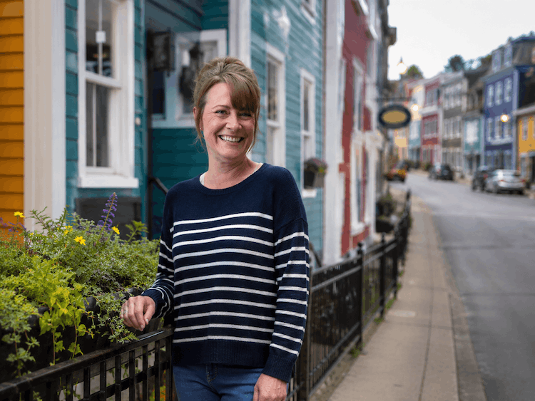 A woman standing on a sidewalk next to colorful houses and smiling.